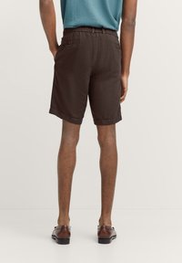 Braune Leinen-Shorts mit einem elastischen Bund, Gesäßtaschen und einem lockeren Schnitt, kombiniert mit braunen Loafers und einem blauen Hemd.