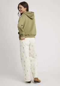 Sweat à capuche vert olive associé à un pantalon large crème avec des motifs de feuilles brunes. Des bottines à talons marron complètent le look.