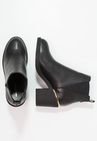 Botines de cuero negro con punta redonda, paneles laterales elásticos y un tacón grueso y texturizado con un acento dorado.