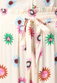 Light fabric with a beige background, featuring colorful floral patterns in pink, green, blue, and brown. Includes a gathered elastic waistband.