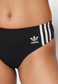Czarne kąpielówki z trzema białymi paskami po bokach. Posiadają haftowane białe logo Adidas. Wykonane z gładkiego, elastycznego materiału.