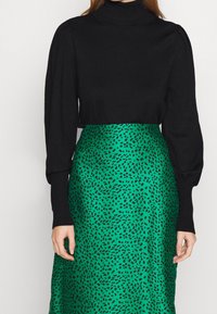 Maglione a collo alto nero con maniche a sbuffo abbinato a una gonna in satin verde con un motivo astratto nero.