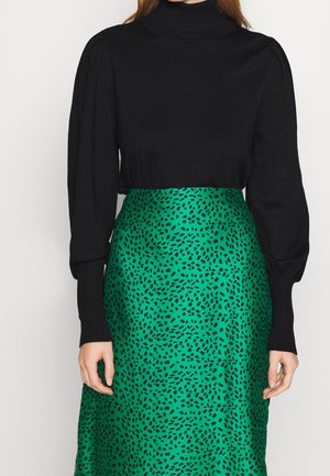 Maglione a collo alto nero con maniche a sbuffo abbinato a una gonna in satin verde con un motivo astratto nero.