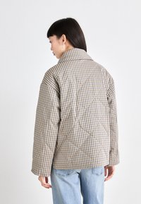 Giacca trapuntata beige con motivo a quadri, dotata di ampio colletto e spalle scese. Texture morbida e vestibilità casual.