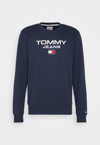 Námořnická mikina se širokým výstřihem, dlouhými rukávy a žebrovanými manžetami. Na přední straně se nachází bílý nápis "TOMMY JEANS" nad malým obdélníkovým detailem loga.