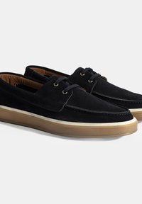 Chaussures en nubuck bleu marine avec un bout arrondi, semelle en caoutchouc beige et deux œillets en métal pour les lacets. Design minimaliste avec des coutures contrastées.