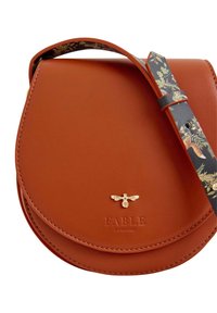 Braune Leder-Crossbody-Tasche mit einem runden Klappenverschluss, goldenen Bienen-Hardware und einem blumenbedruckten Tragegurt. Mit eingeprägtem Markenlogo.