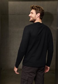 Black long-sleeve t-shirt made from soft material, featuring a crew neck design. Paired with dark cargo pants. Subtle texture visible.