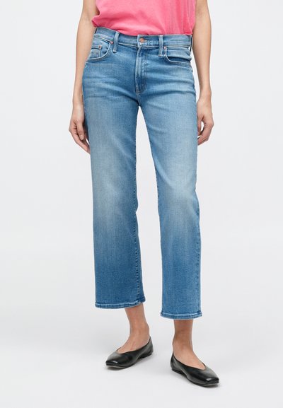 Plave traperice ravnog kroja, blago izblijedjele, s dva prednja džepa i gumbima na preklop; uparene s crnim baletankama i ružičastom majicom.