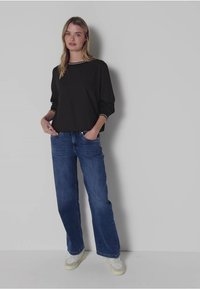 Zwarte lange mouwen top met witte accentafwerking gecombineerd met blauwe wijde jeans en witte sneakers. Eenvoudig ontwerp, casual uitstraling.