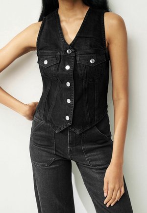 Gilet en denim noir avec un col en V, des boutons en argent et deux poches avant. Design ajusté qui souligne la taille, associé à un pantalon assorti de couleur sombre.