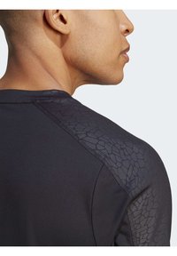 Schwarzes Sportshirt mit strukturierten Details an der Schulter, aus ribbeligem Stoff und mit taillierter Passform, geeignet für aktive Freizeit.