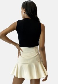 Top de rayas negro sin mangas combinado con una falda corta acampanada color crema. El conjunto presenta una textura suave y una silueta ajustada.