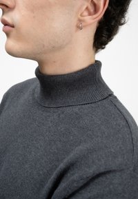 Graüer Rollkragensweater mit geripptem Kragen, figurbetontem Design und weicher Textur. Nahaufnahme, die den Ausschnitt und den Schulterbereich hervorhebt.