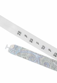 Maßband aus weißem Stoff mit schwarzen Größenangaben. Ein dekorativer Stoffstreifen in Grau mit blauen Wirbeln ist angebracht.