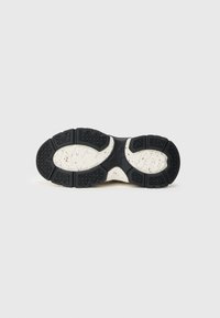 Suela exterior de zapato deportivo en blanco y negro con goma negra texturizada, forma contorneada, patrón de banda de rodadura prominente y media suela blanca salpicada.