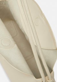 Beżowa skórzana torba wewnętrzna z gładką teksturą, zamknięciem na zamek i okrągłymi akcentami. Podszewka wykonana jest z miękkiego, jasnego materiału.