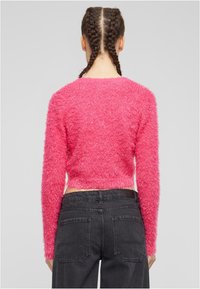Avskuren rosa fluffig tröja med långa ärmar, med en mjuk textur och rundad halsringning, i kombination med högmidjade svarta jeans.