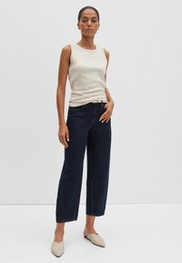 Débardeur beige à côtes, jeans large foncé et mules de couleur claire. L'ensemble présente un haut ajusté et une silhouette en denim décontractée.