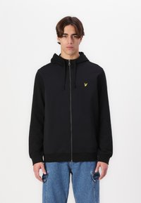 Sudadera con cremallera negra y capucha ajustable, que presenta un pequeño logotipo amarillo en el pecho. Tejido suave, puños y dobladillo acanalados.