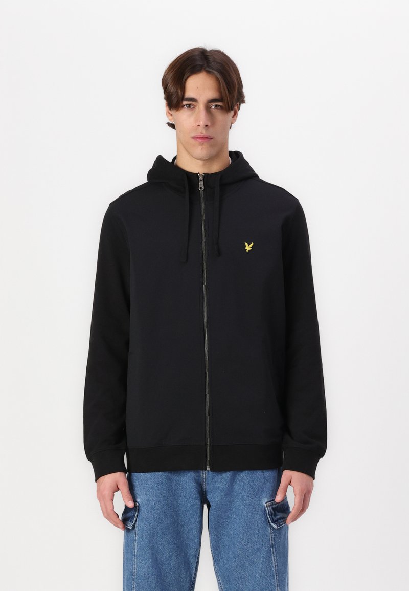 Sudadera con cremallera negra y capucha ajustable, que presenta un pequeño logotipo amarillo en el pecho. Tejido suave, puños y dobladillo acanalados.