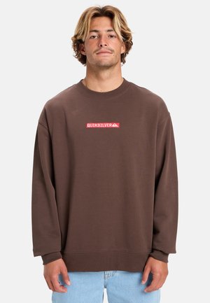 Bruine oversized sweatshirt met een ronde hals en lange mouwen. Heeft een rood rechthoekig Quiksilver-logo op de borst. Zachte stoftextuur.