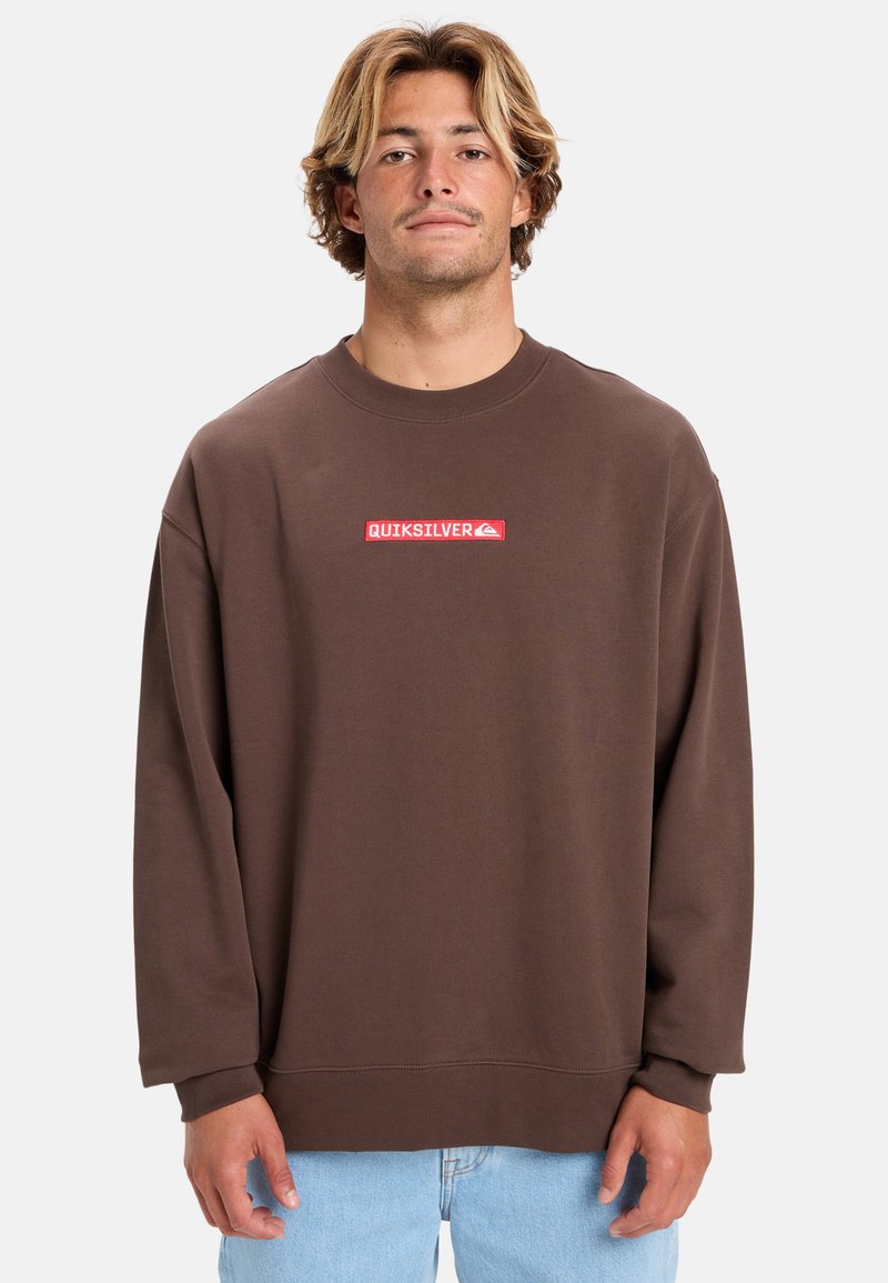 Bruine oversized sweatshirt met een ronde hals en lange mouwen. Heeft een rood rechthoekig Quiksilver-logo op de borst. Zachte stoftextuur.