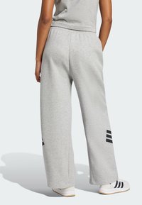 Jasnoszare szerokie dresy z elastycznym paskiem w talii, z czarnymi paskami z logo przy dolnej krawędzi. Wykonane z miękkiego, teksturowanego materiału.