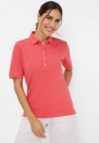 Korte ærmer koralfarvet polo skjorte lavet af letvægtsstof med en knappet placket og en lille logo aksent ved kanten.