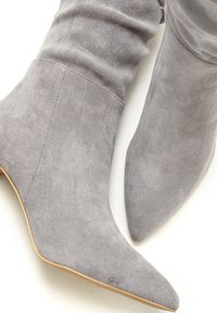 Gray suede ankle boots with a slouchy design, pointed toes, and smooth texture. Features a minimalistic style with no visible hardware.