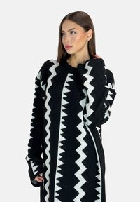 Pull en maille noir et blanc à motifs zigzag, manches longues et coupe décontractée avec encolure et poignets côtelés.