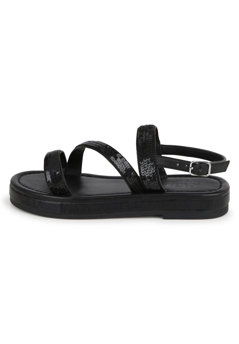 Sandales noires à semelle plate, avec des brides croisées pailletées et une boucle réglable à la cheville. Semelle intérieure en cuir lisse et design minimaliste.