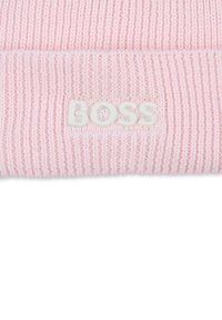 Bonnet tricoté rose clair avec une texture côtelée et un logo "BOSS" brodé en blanc à l'avant. Matériau doux et extensible.