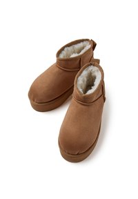 Botas de tobillo de ante marrón con un suave forro de piel sintética blanca, punta redondeada y una lengüeta en la parte posterior para ponerlas fácilmente.