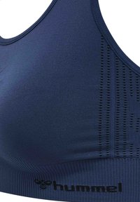 Granatowy biustonosz sportowy z oddychającymi bocznymi panelami z siateczki i czarnym logo "hummel" na prążkowanym pasie pod biustem.