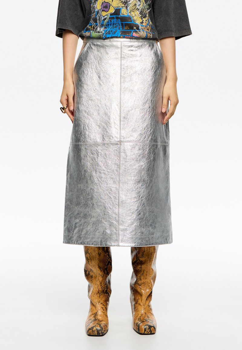 Zilveren metallic midi-skirt met een gladde textuur en naaddetails, gecombineerd met kniehoge laarzen met slangenprint.