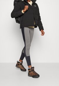 Person som går och bär mörkbruna vandringsskor, grå och svarta leggings, en svart puffjacka och en svart ryggsäck.