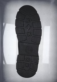 Czarna gumowa podeszwa buta z głębokim wzorem bieżnika, okrągłym obcasem i podniesionymi akcentami. Wyśrodkowane logo z okrągłym wzorem.