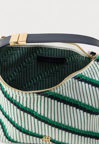 Wiklinowa torba na ramię w zielono-biały wzór w paski, z złotym zamkiem błyskawicznym i usztywnionym kształtem. Wnętrze wyłożone zieloną tkaniną.