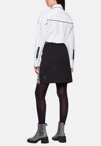 White shirt with navy accents, black skirt with patterned side panel, and gray ankle boots, worn above dark tights. Simple, modern design.
