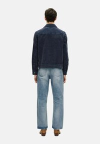 Marineblå denimjacka med kypertfinish, med en traditionell krage, långa ärmar och kontrasterande sömmar, i kombination med ljusblå jeans.