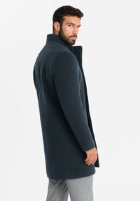 Cappotto di lana blu navy con colletto alto, design monopetto e vestibilità sartoriale, caratterizzato da linee eleganti e minimaliste.