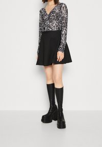Langärmliges Oberteil mit einem schwarz-weißen abstrakten Muster, kombiniert mit einem schwarzen ausgestellten Rock und knielangen schwarzen Stiefeln mit Absatz.