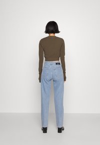 Vihreä, vyötäröltä lyhennetty pitkähiha-paita, yhdistetty vaaleansinisiin korkeavyötäröisiin farkkuihin. Mustat nilkkurit. Yksinkertainen muotoilu, tasaiset pinnat.