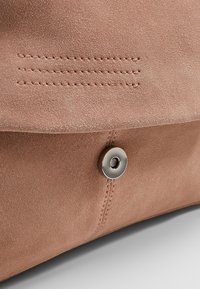 Růžová semišová taška s magnetickým uzávěrem, zdobená šitými liniemi a hladkým povrchem. Minimalistický design s jemnými akcenty.