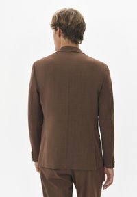 Pruun kohandatud ülikonna jakk sujuva tekstuuriga, ühe tagumise lõhiku ja sobivate pükstega, esitledes modernset ja minimalistlikku disaini.