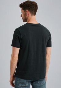 Čierne bavlnené tričko s okrúhlym výstrihom a krátkymi rukávmi. Zadná strana má hladkú textúru a žiadne viditeľné logá ani dizajny. Nosené s modrými džínsami.