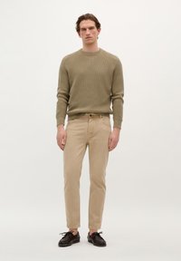 Jersey de punto acanalado beige, pantalones beige ajustados y zapatos oscuros. Paleta de colores neutros, tejido texturizado y diseño casual.