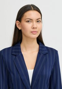 Tengerészkék csíkos blazer, kivágott gallérral, fehér csíkokkal és szerkezetes fazonnal, sima anyagból készült.