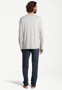 Grijze langemouwen shirt gecombineerd met donkerblauwe broek, met een relaxte pasvorm en zachte stof. Achteraanzicht toont een eenvoudig ontwerp, zonder patronen.